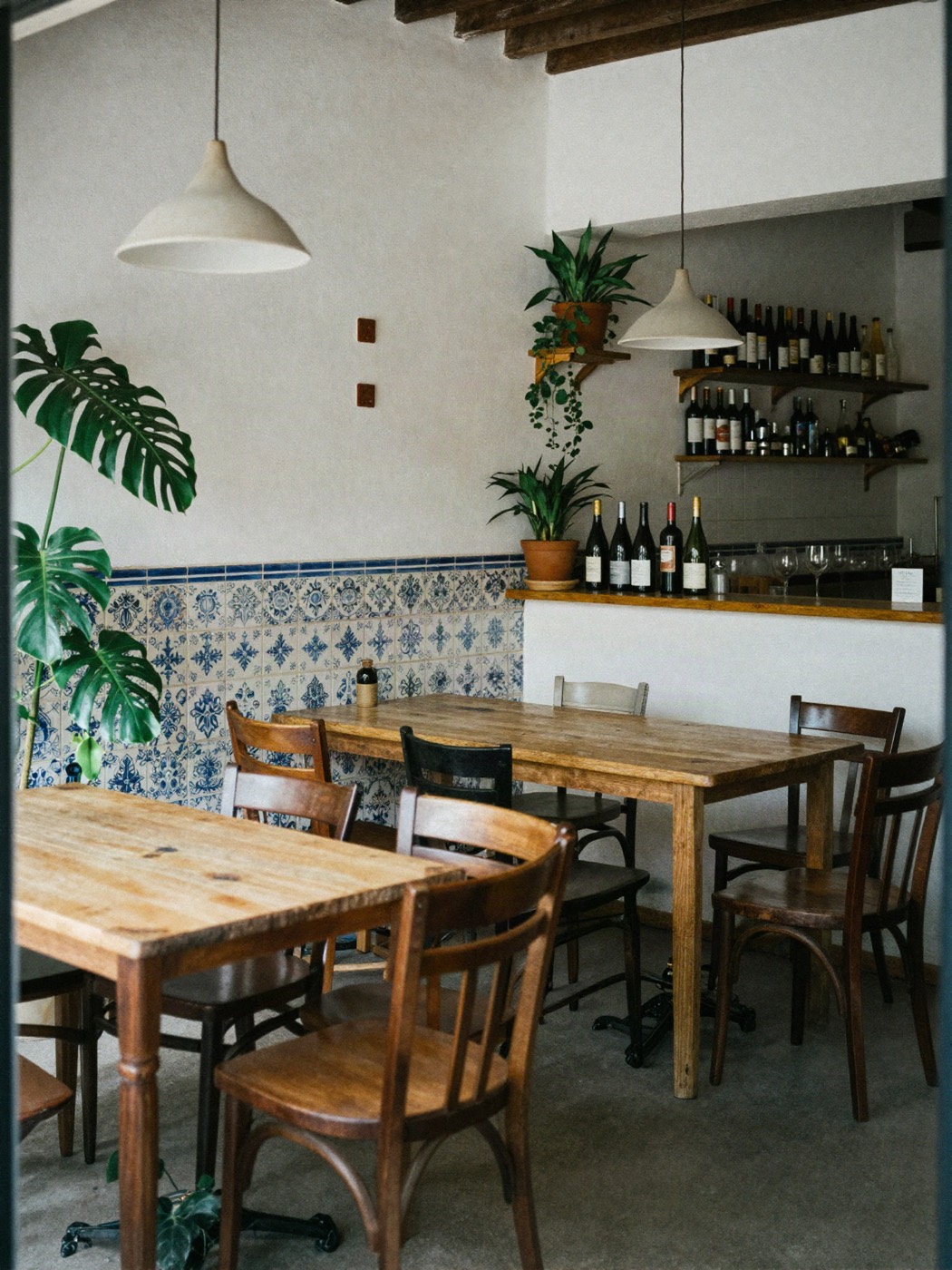 Comedor pequeño con mesas de madera, azulejos valencianos azules, plantas y una barra con botellas de vino